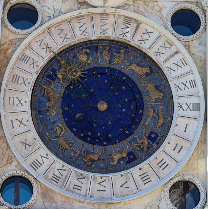 A detailed view of the historic astrological clock in Venice, featuring zodiac signs and Roman numerals.