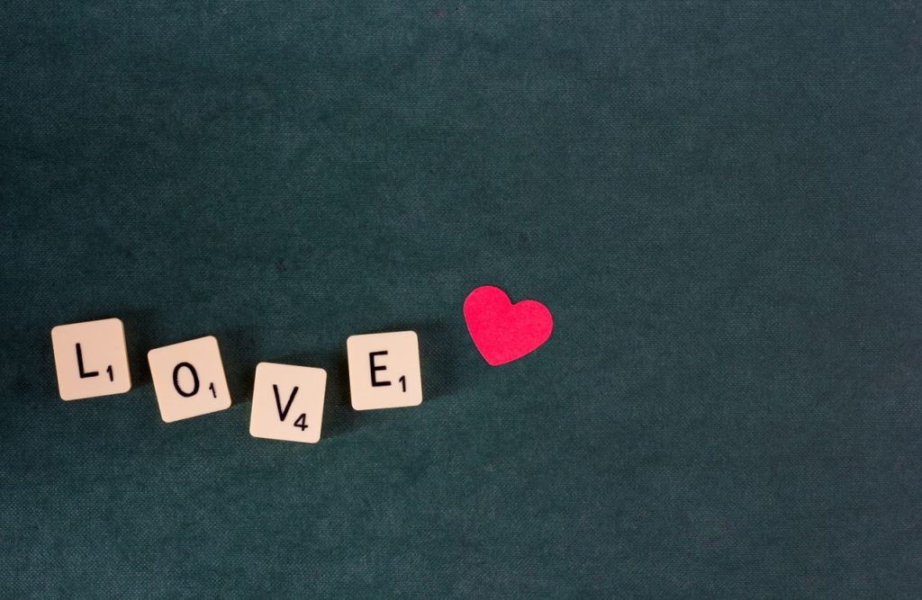 Scrabble tiles forming the word 'LOVE' with a red heart on a green background.