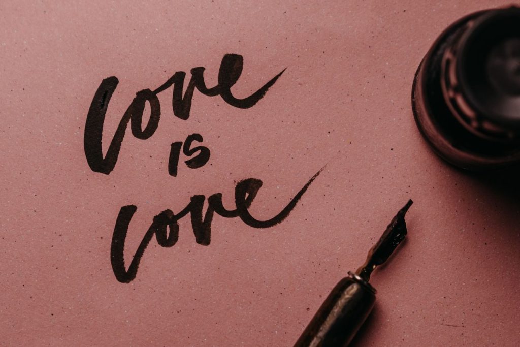 Beautiful hand lettering 'Love is Love' on a pink paper with ink pen.